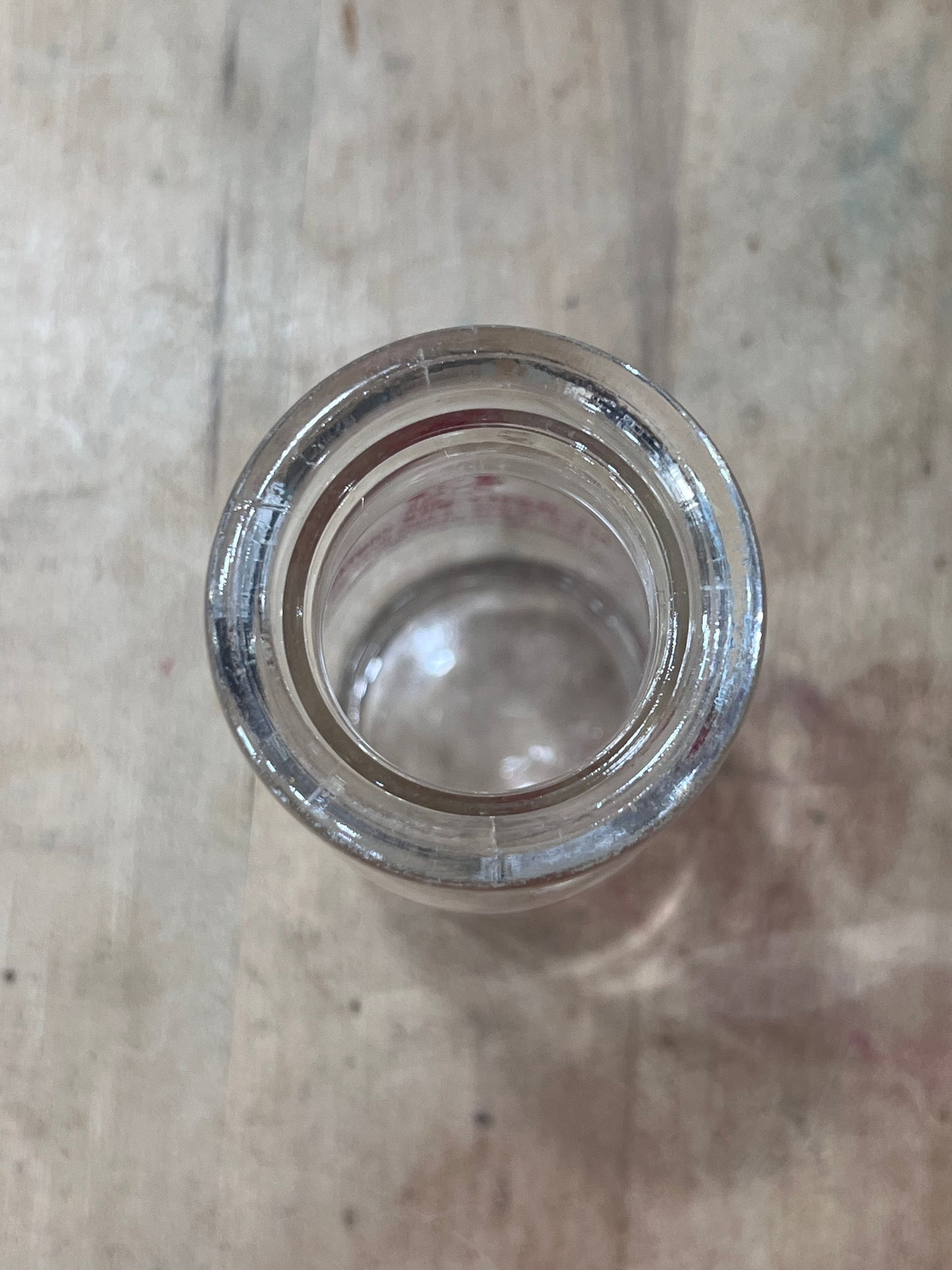 A clear glass bottle viewed from above, showing the circular glass opening and a small amount of white residue or sediment inside, set against a light gray textured background.