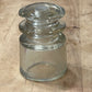 A clear glass electrical insulator with a flared base and rounded side, lying on a light brown wooden surface.