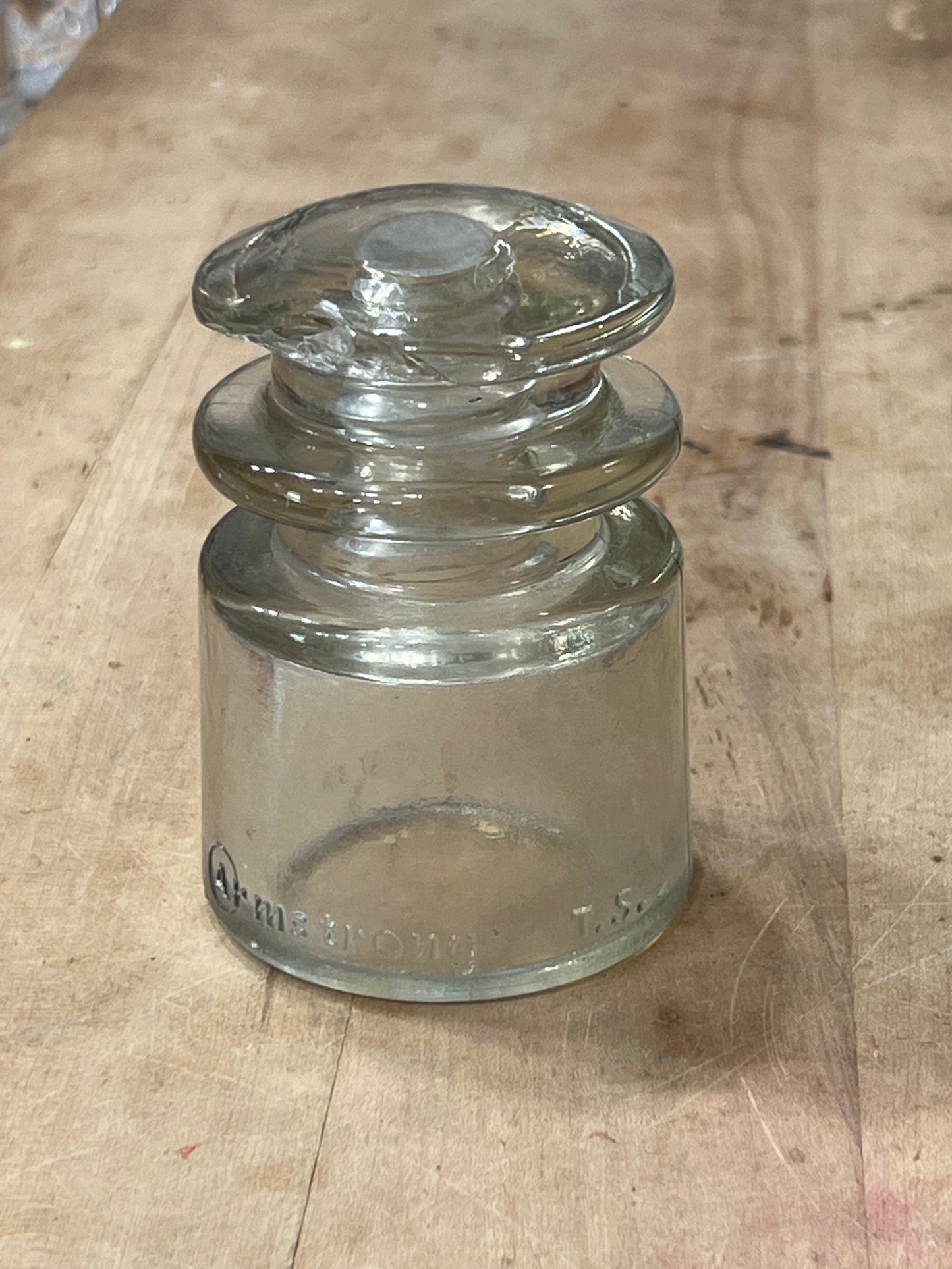 A clear glass electrical insulator with a flared base and rounded side, lying on a light brown wooden surface.