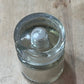 A clear glass jar with a screw-on lid, lying on its side on a light-colored wooden surface.