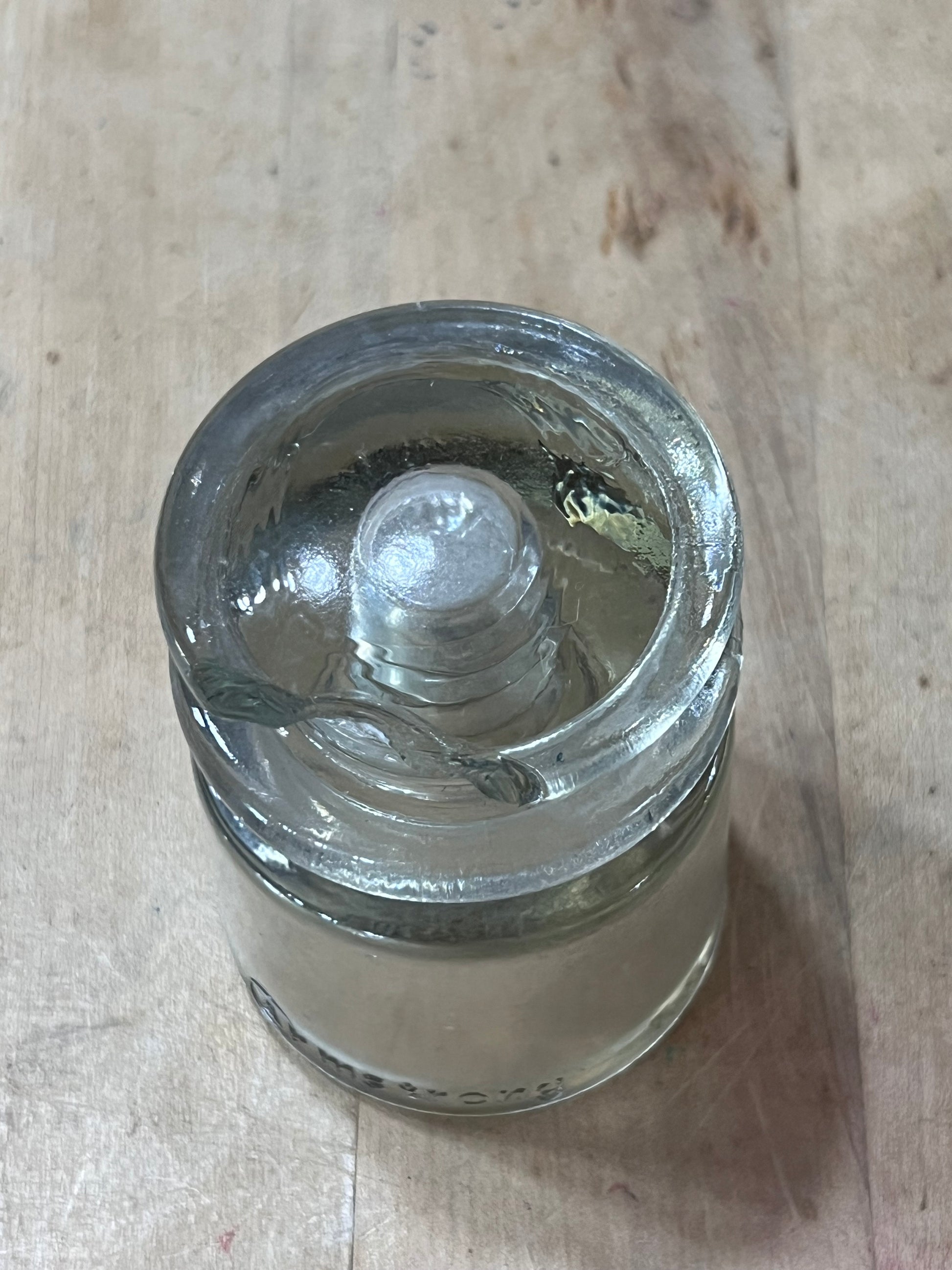 A clear glass jar with a screw-on lid, lying on its side on a light-colored wooden surface.