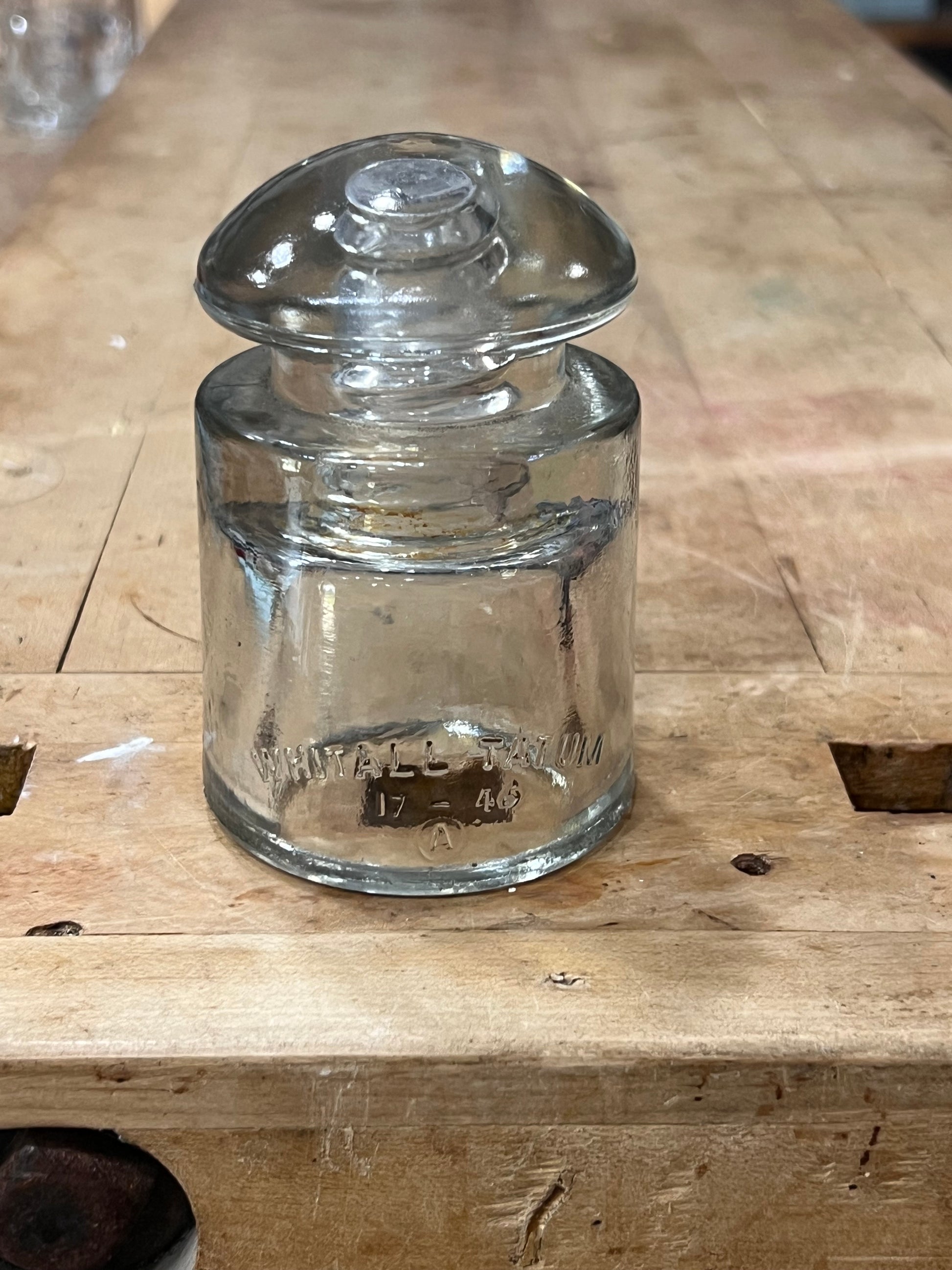 A clear glass insulator bulb, likely a vintage electrical or laboratory glass piece, lying on a rustic wooden workbench.