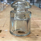 A clear glass apothecary jar with a matching screw-top lid, resting on a wooden surface.