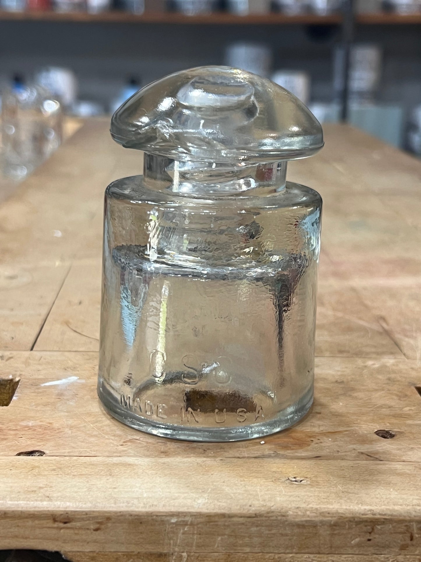A clear glass apothecary jar with a matching screw-top lid, resting on a wooden surface.