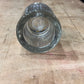 A clear glass bottle stopper or cap with a textured, ribbed outer ring and a smooth, domed center, shown from a top-down perspective on a worn wooden tabletop.