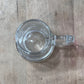 A clear glass mug with a handle, viewed from above on a light brown wooden surface.