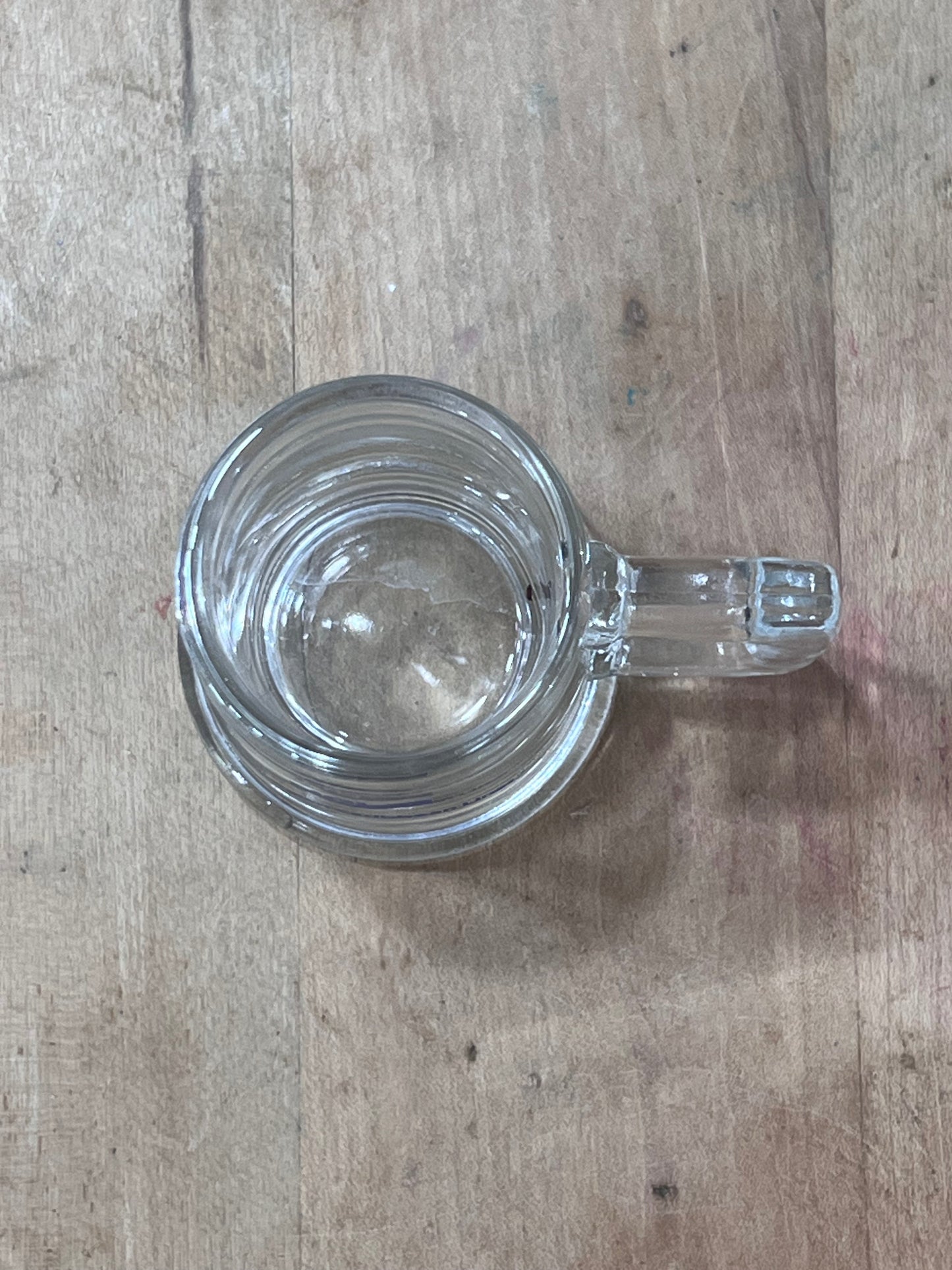 A clear glass mug with a handle, viewed from above on a light brown wooden surface.