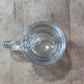 A clear glass mug with a thick handle, viewed from directly above on a light brown wooden surface.