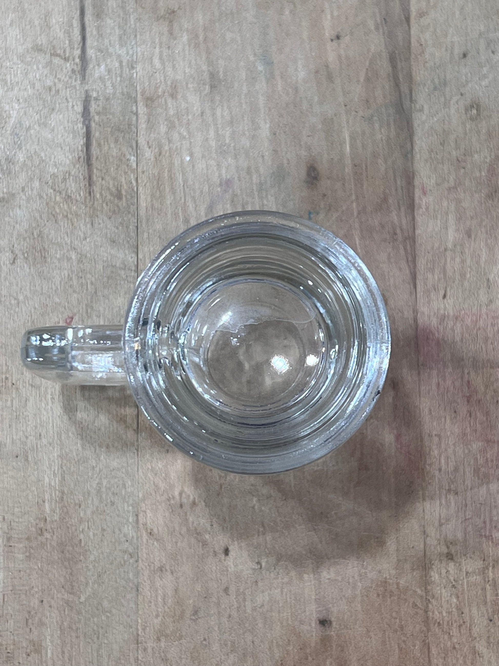 A clear glass mug with a thick handle, viewed from directly above on a light brown wooden surface.