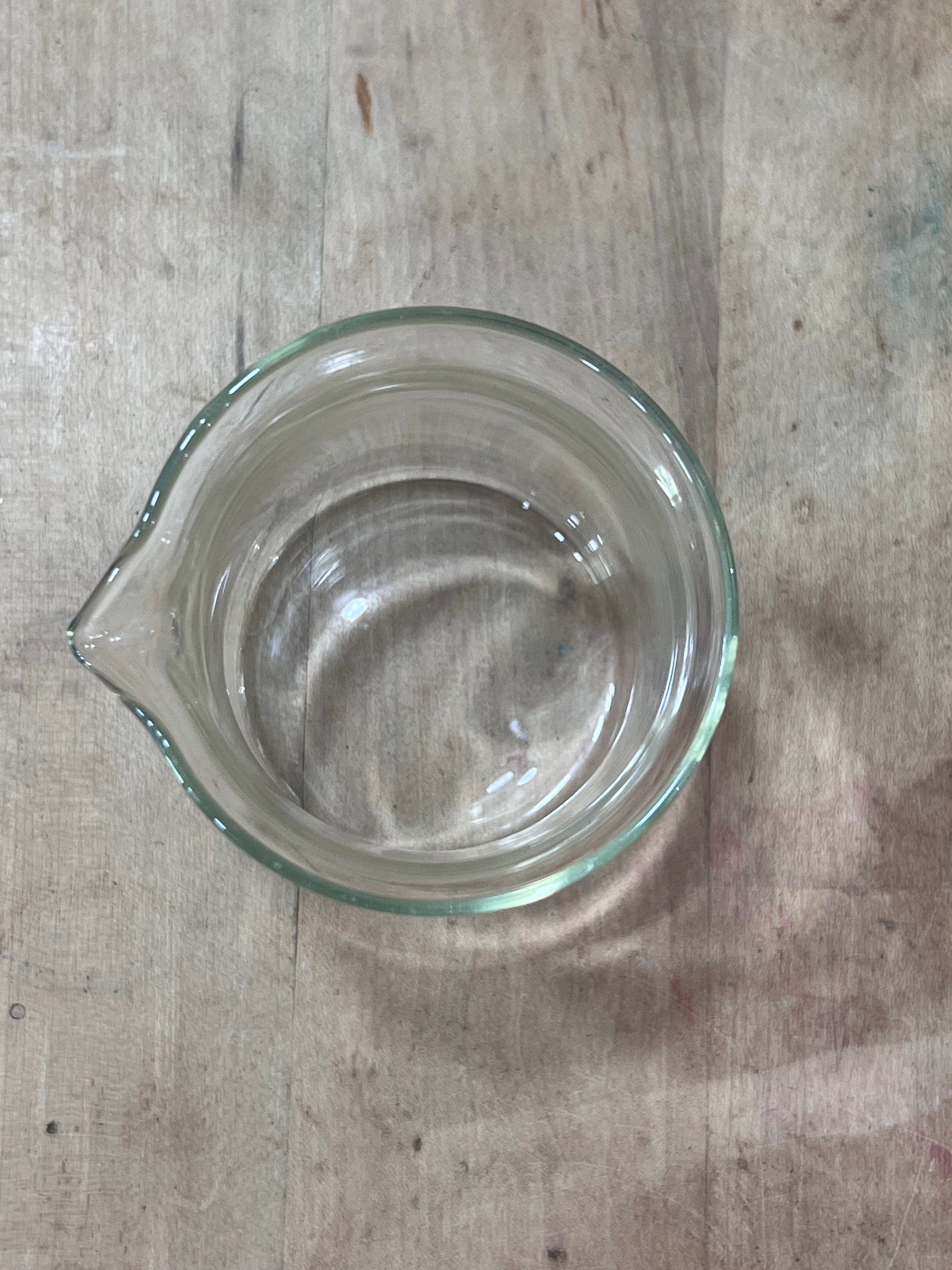 A clear glass measuring cup with a pouring spout, viewed from directly above on a rustic wooden surface.