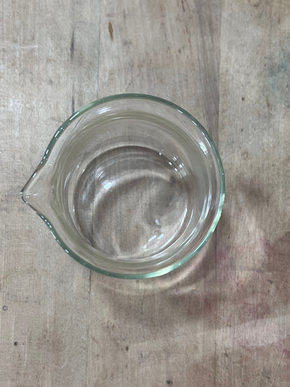 A clear glass measuring cup with a pouring spout, viewed from directly above on a rustic wooden surface.