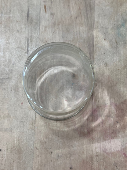 A clear glass jar with a matching clear lid, viewed from directly above on a light-colored wooden surface.