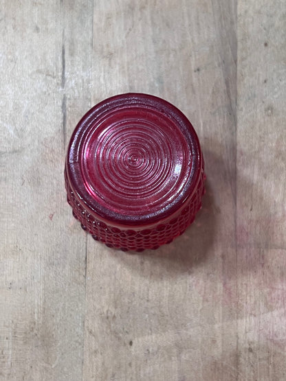 A red textured glass tumbler viewed from above, showing a concentric circular pattern on the flat top and a honeycomb-style textured base, placed on a light wood surface.