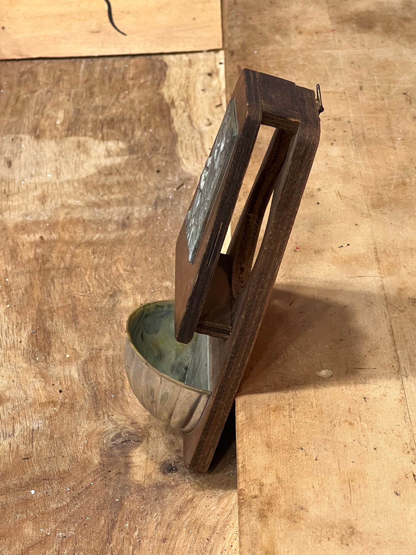 A dark brown wooden wall-mounted frame holding a small vertical artwork, photographed on a rustic wooden tabletop.