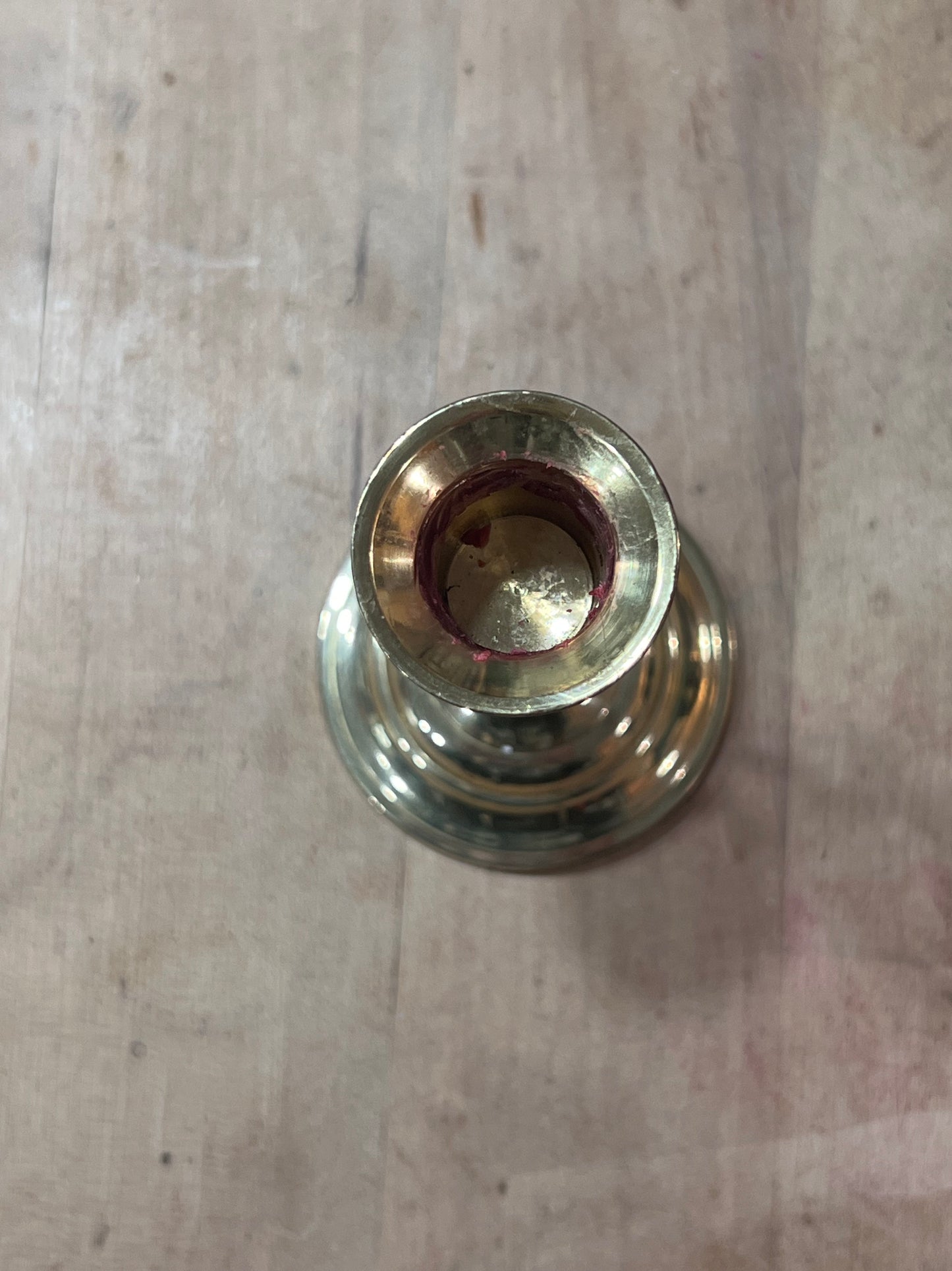A close-up top-down view of a brass candle holder or vase base with a reddish-brown wax residue inside the opening, set on a light wood surface.