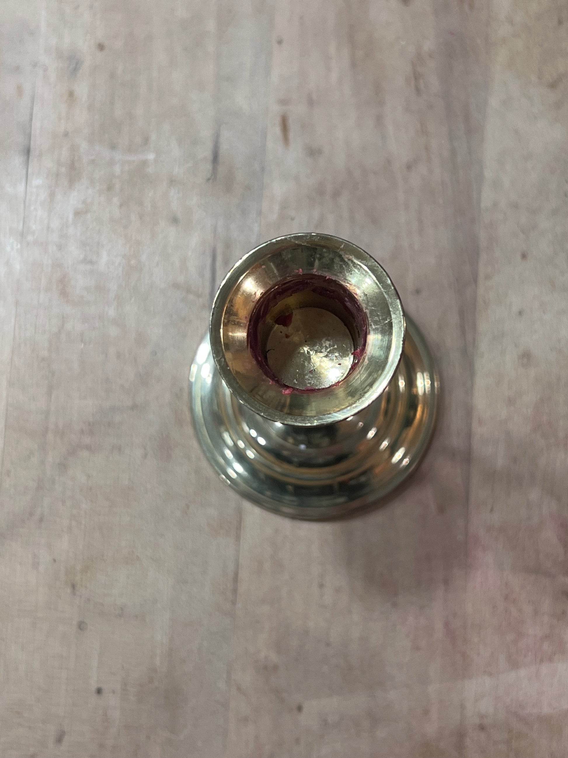 A close-up top-down view of a brass candle holder or vase base with a reddish-brown wax residue inside the opening, set on a light wood surface.