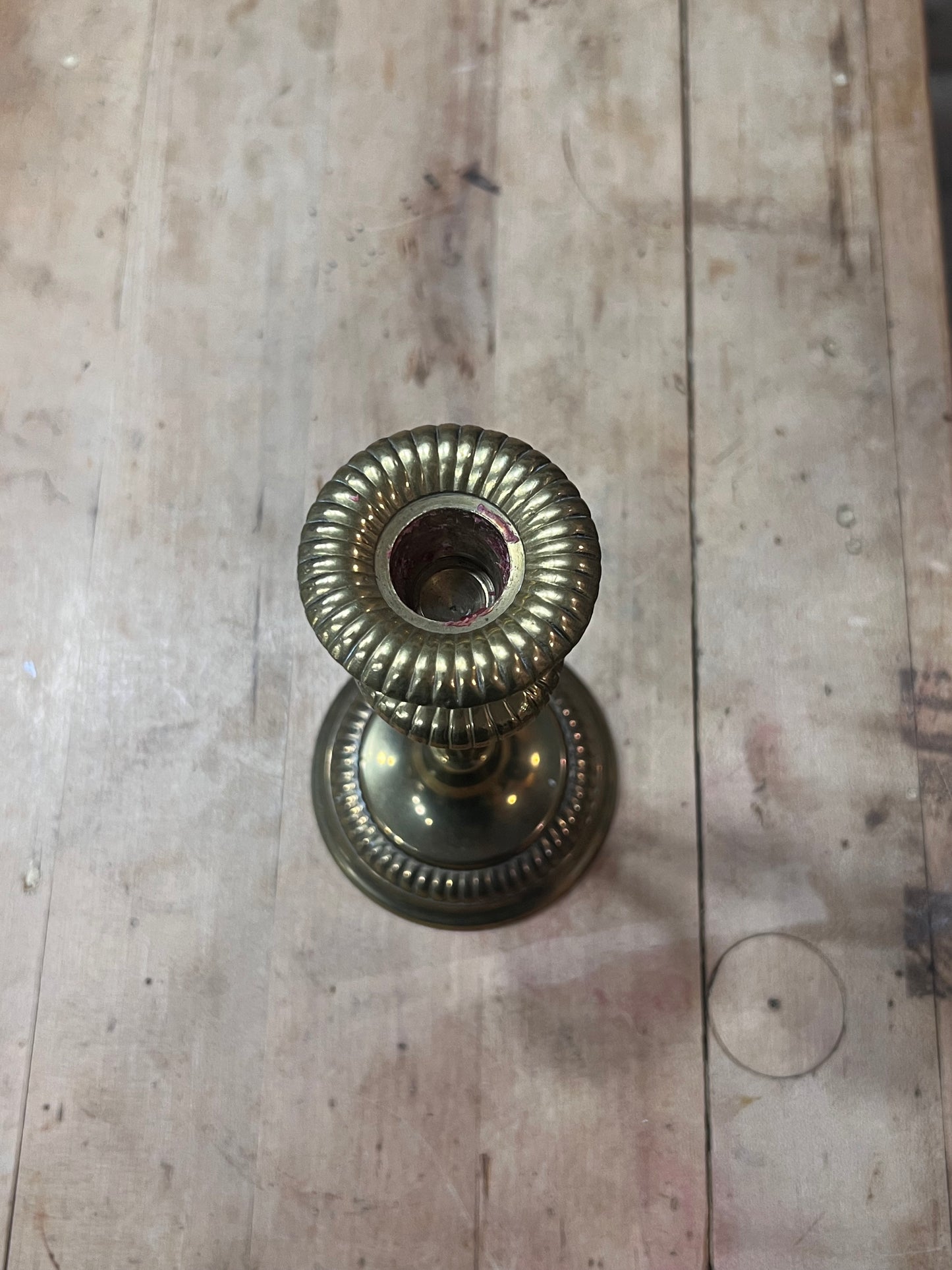 A vintage brass candlestick holder with a ribbed circular top and matching base, photographed from above on a weathered wooden surface.
