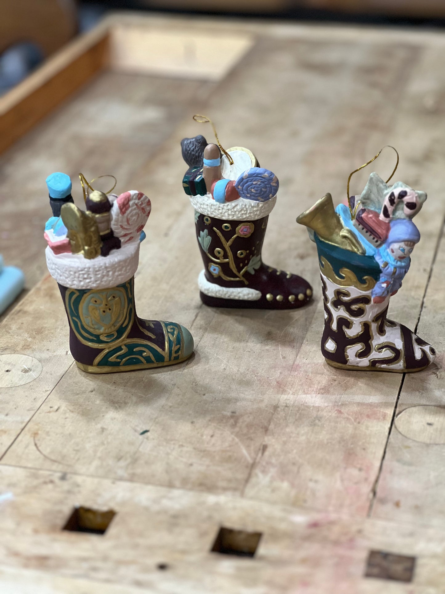 Three hand-painted Christmas stockings ornaments filled with miniature holiday items, displayed on a wooden surface.