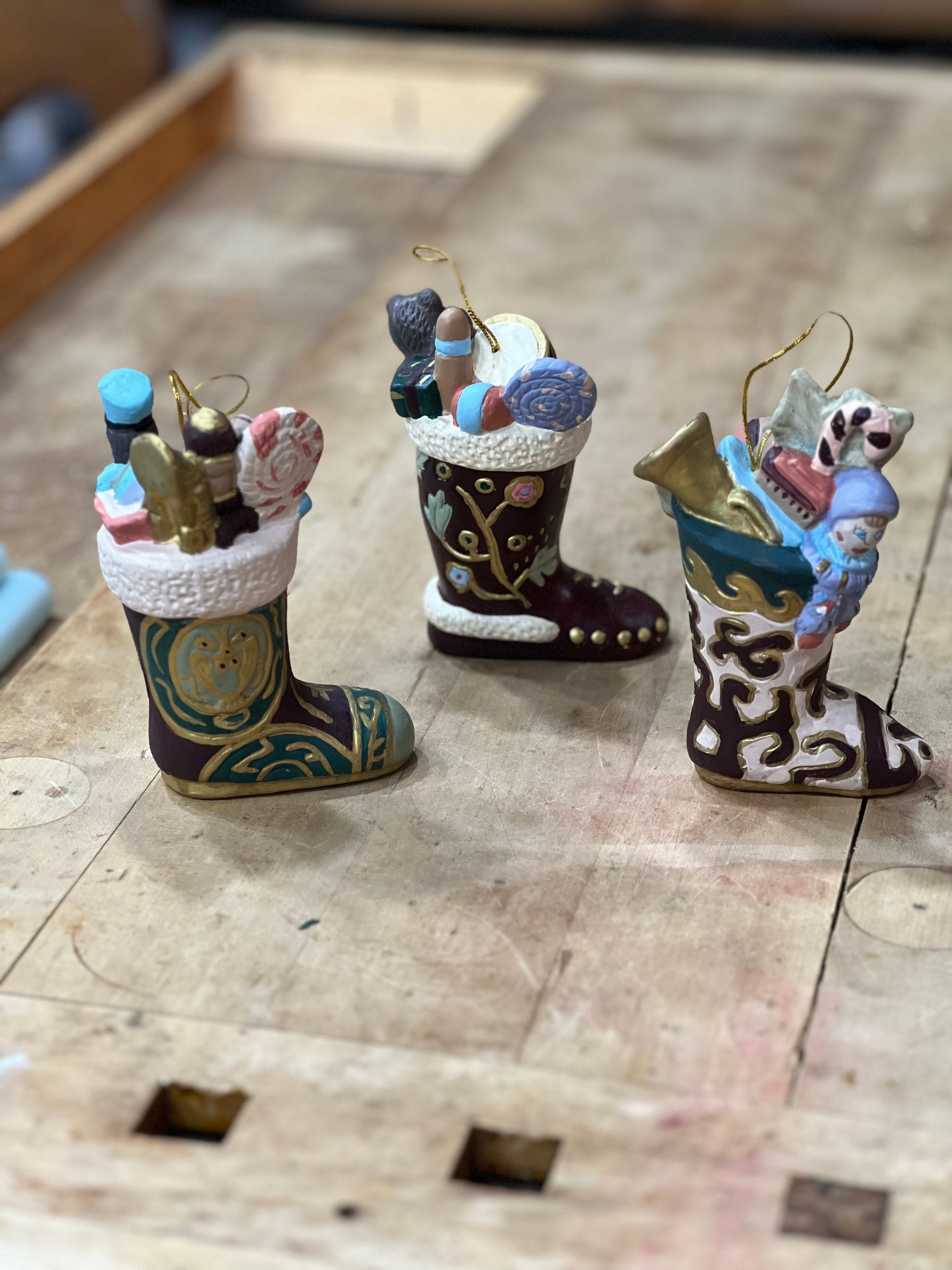 Three hand-painted Christmas stockings ornaments filled with miniature holiday items, displayed on a wooden surface.