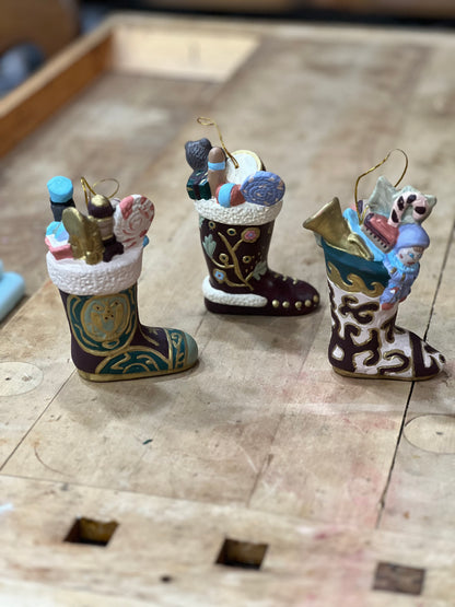 Three hand-painted Christmas stockings ornaments filled with miniature holiday items, displayed on a wooden surface.