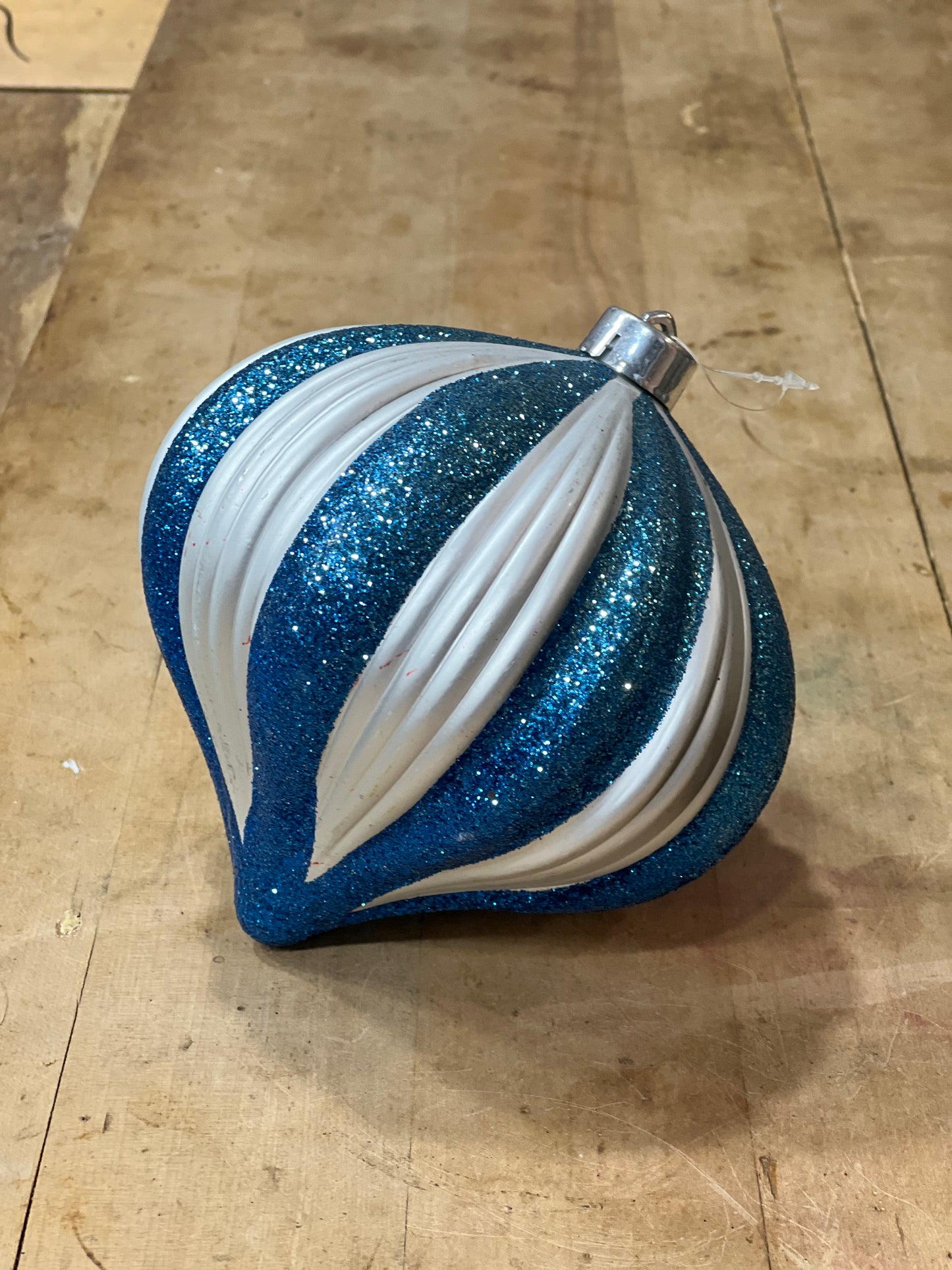 A blue and white striped Christmas ornament with glitter and ribbed texture, resting on a wooden surface.