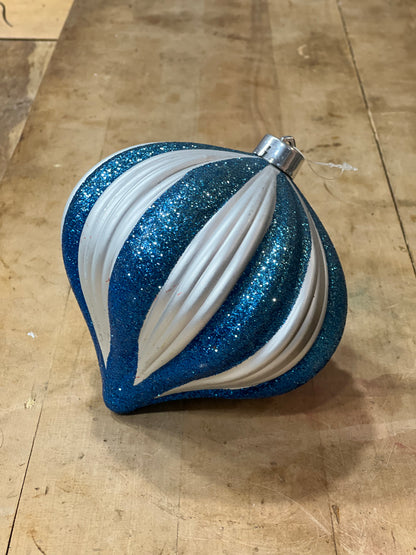 A blue and white striped Christmas ornament with glitter and ribbed texture, resting on a wooden surface.