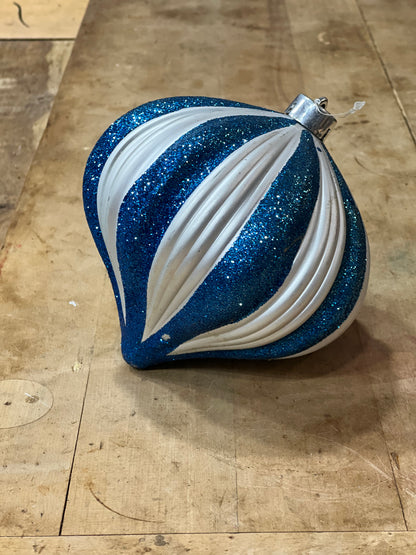 A blue and white striped Christmas ornament with glitter and ribbed detailing, resting on a wooden surface.