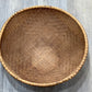 A round woven rattan basket with a natural brown color, photographed from a top-down perspective on a gray wood-look floor.