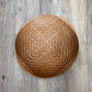 A round woven rattan basket with a textured honeycomb pattern, photographed from directly above on a gray wood plank floor.