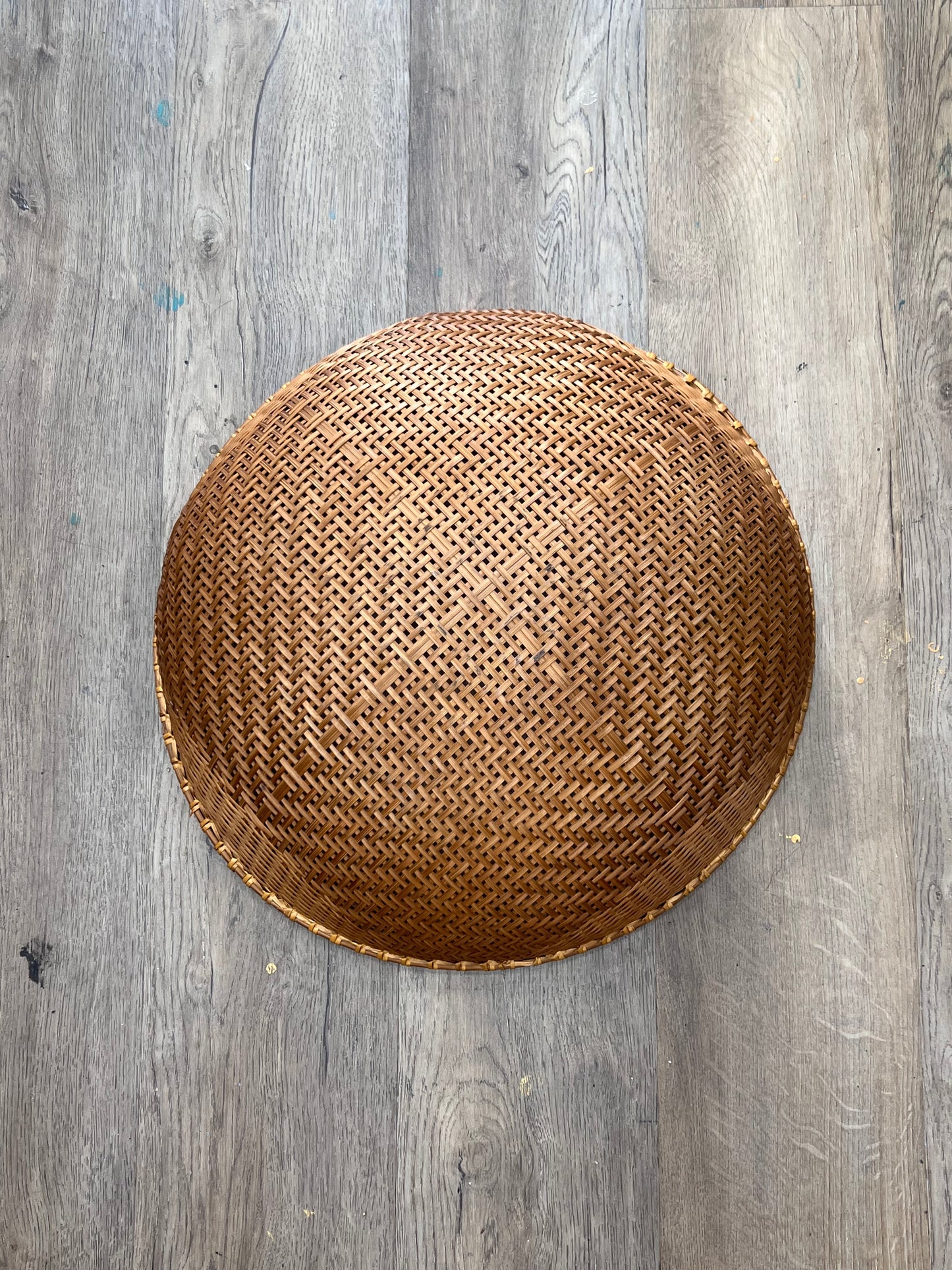 A round woven rattan basket with a textured honeycomb pattern, photographed from directly above on a gray wood plank floor.