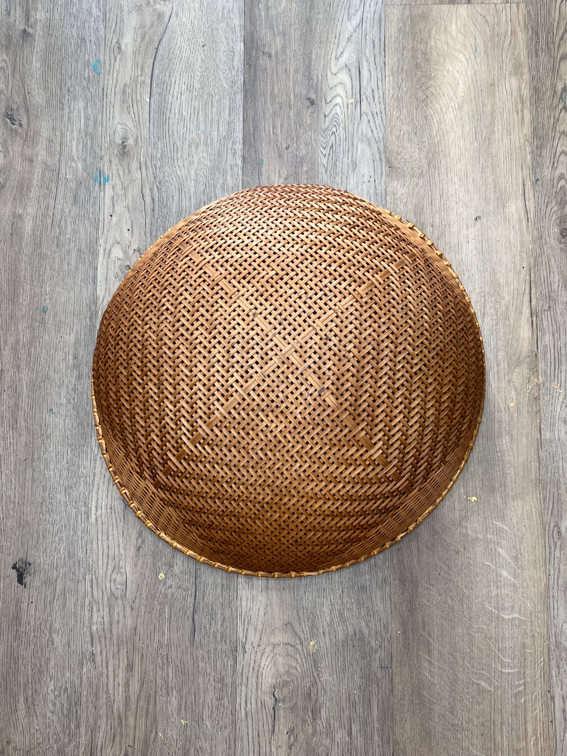 A round woven rattan basket with a textured honeycomb pattern, photographed from directly above on a gray wood plank floor.