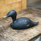 A hand-painted black wooden duck deco with a natural wood beak, resting on a rustic wooden table.