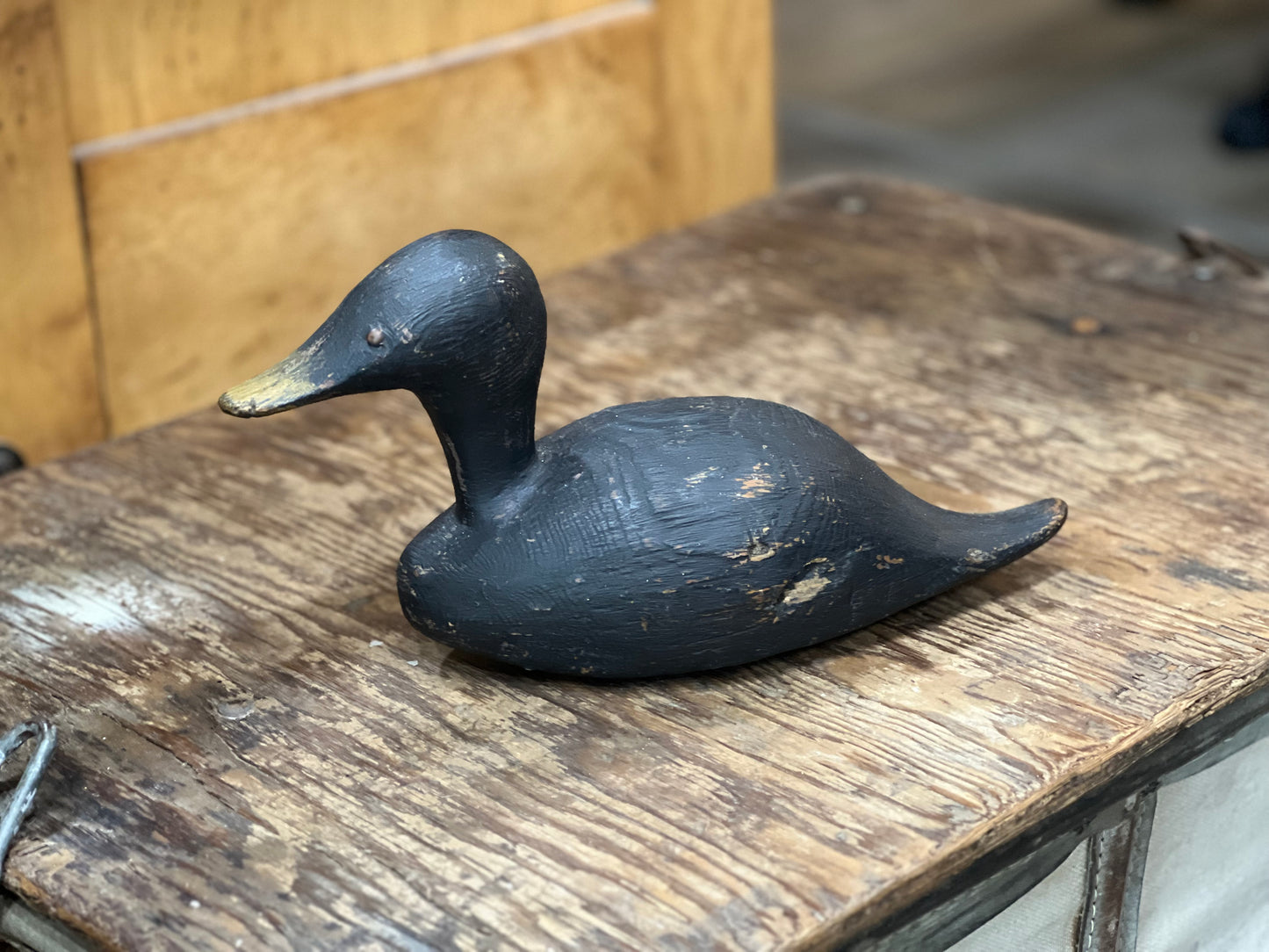 A hand-painted black wooden duck deco with a natural wood beak, resting on a rustic wooden table.