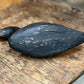 A dark, weathered black wooden duck toy with a natural wood beak, resting on a rustic wooden surface.