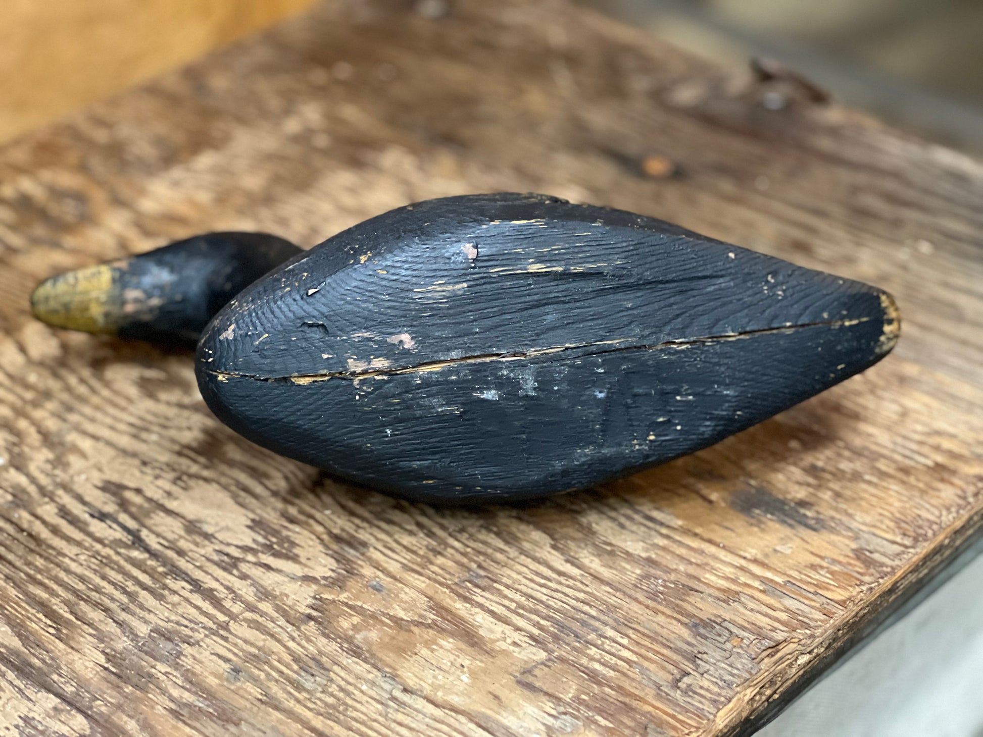 A dark, weathered black wooden duck toy with a natural wood beak, resting on a rustic wooden surface.