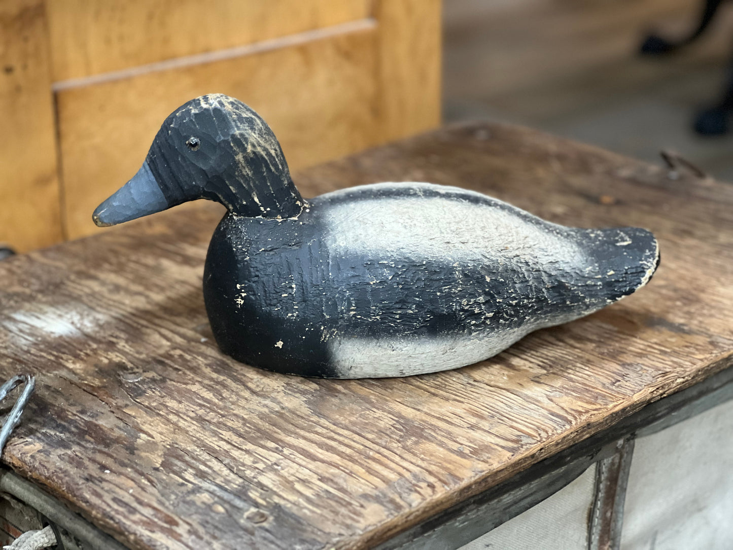 A hand-painted wooden duck deco shaped like a shoveler's duck, featuring a black head and back with a white belly, resting on a rustic wooden table.