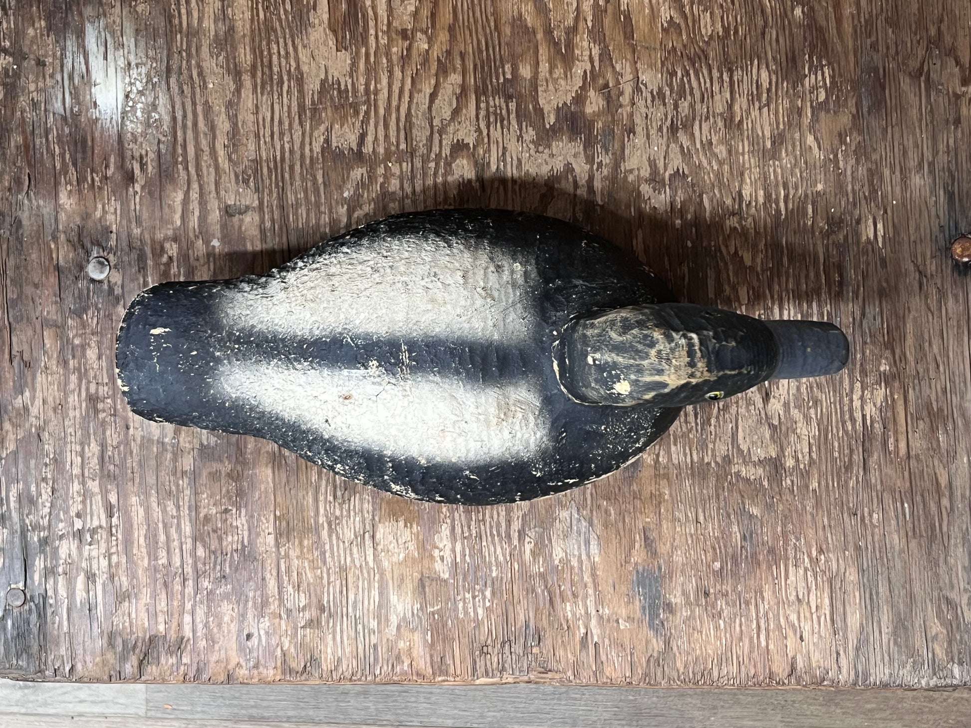 A vintage black and white painted wooden duck deco resting on a rustic, weathered brown wooden surface.