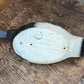 A vintage wooden duck hunting blind or deco, shown from the underside on a rustic wooden table. The body is painted off-white with black tips on the tail and bill, and a gray plastic or metal blade is attached to the tail.