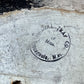 A close-up of a weathered, off-white painted surface with a circular black stamp reading 'Cargoula, Miss. of Miss.