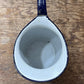 A vintage teardrop-shaped enamel pitcher with a dark blue exterior and white interior, shown from a top-down view on a rustic wooden surface.