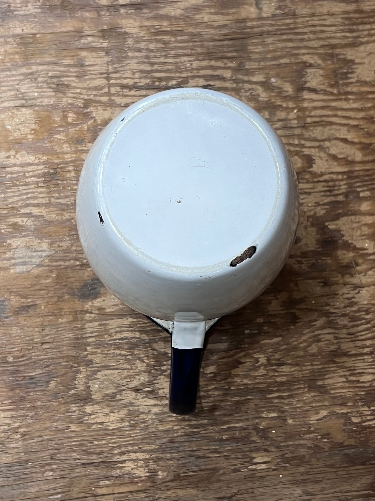 The bottom view of a white ceramic mug with a dark blue handle, resting on a rustic wooden surface.