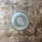 A small clear glass bottle viewed from above, placed on a rustic brown wooden surface.