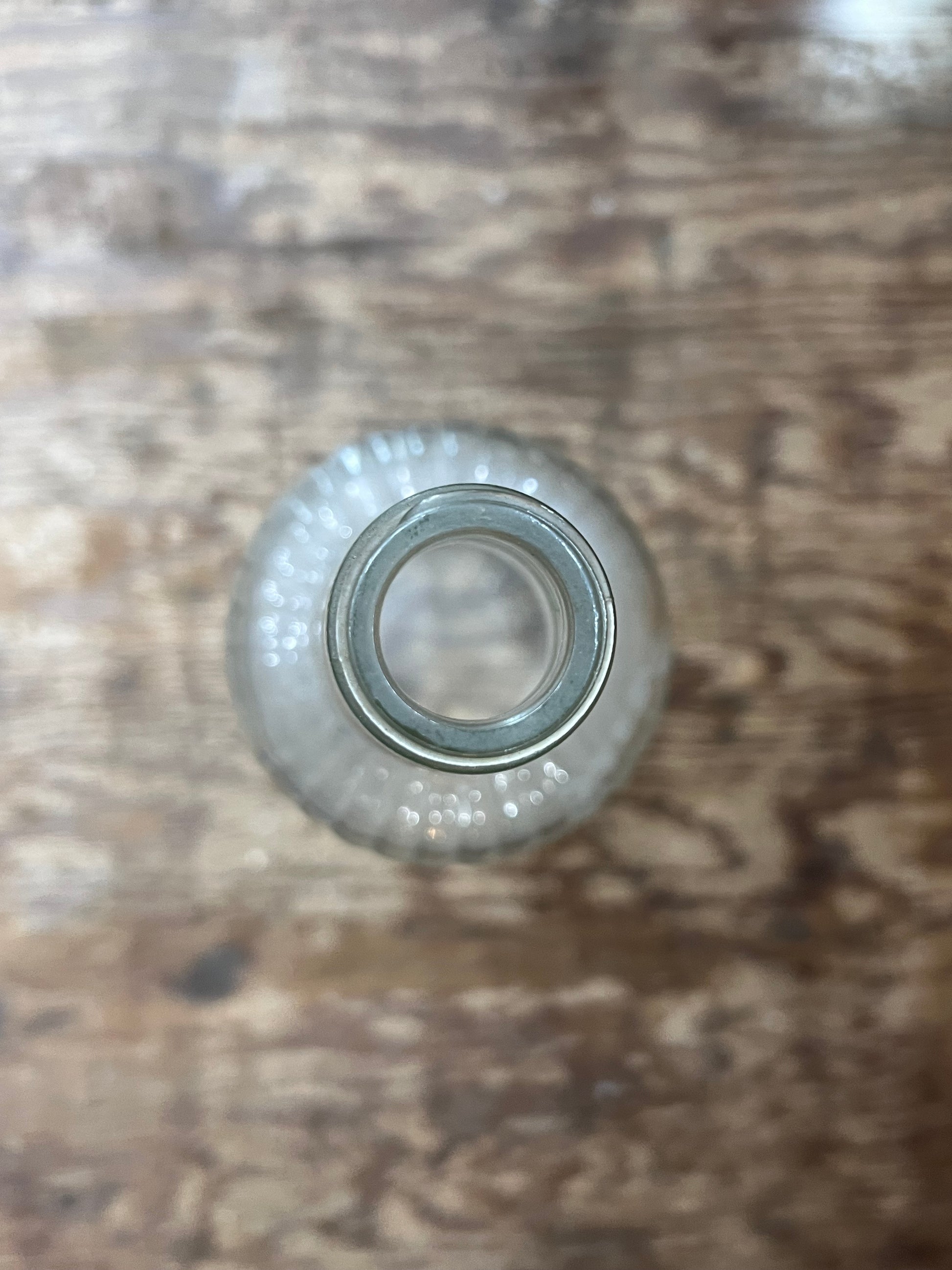 A small clear glass bottle viewed from above, placed on a rustic brown wooden surface.