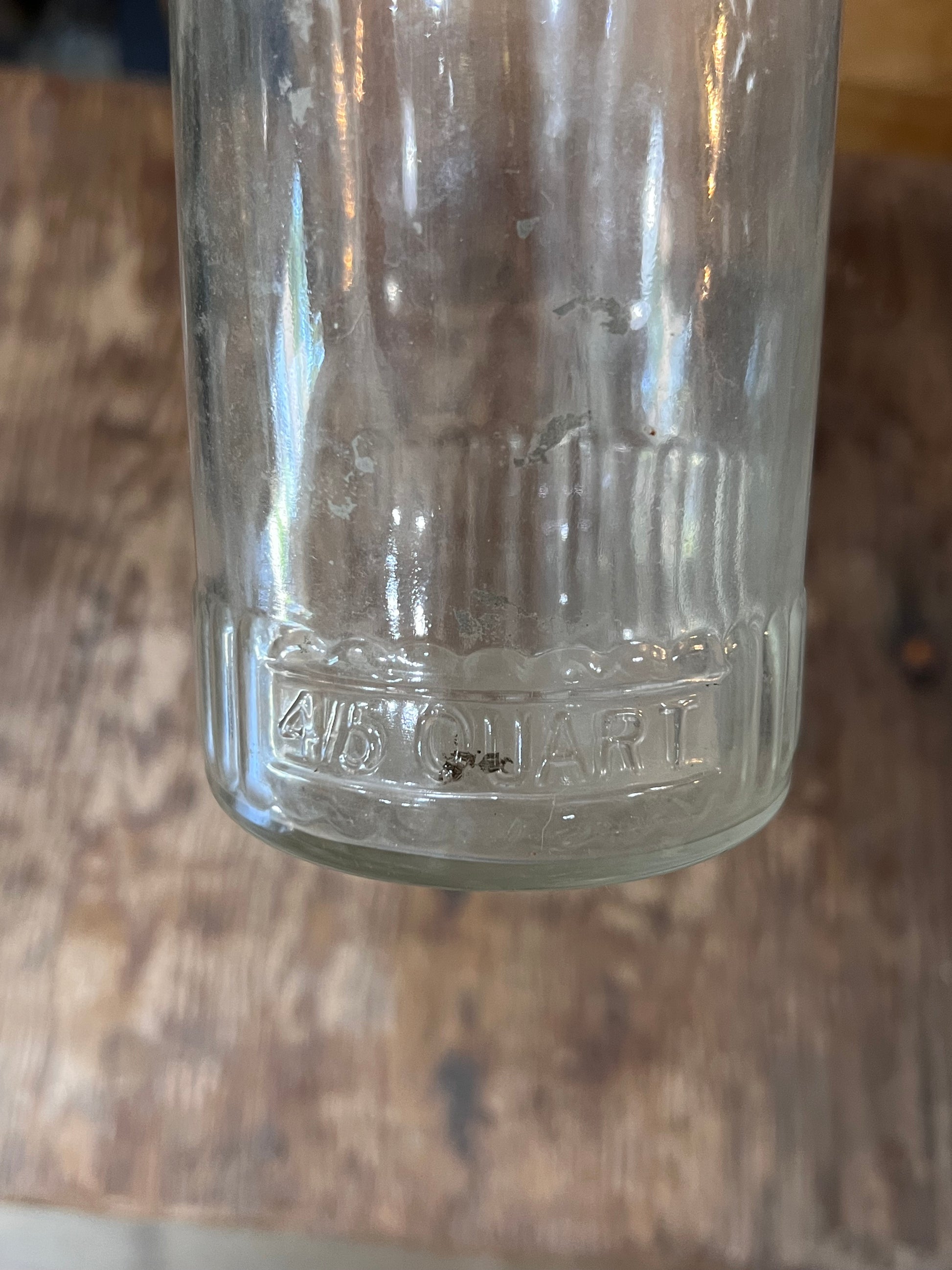 A close-up of a clear glass jar or bottle base embossed with '4 1/2 QUART' on a rustic wooden surface.