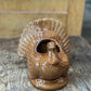 A brown glazed ceramic turkey-shaped planter with a raised fan tail and a central opening, displayed on a rustic wooden surface.