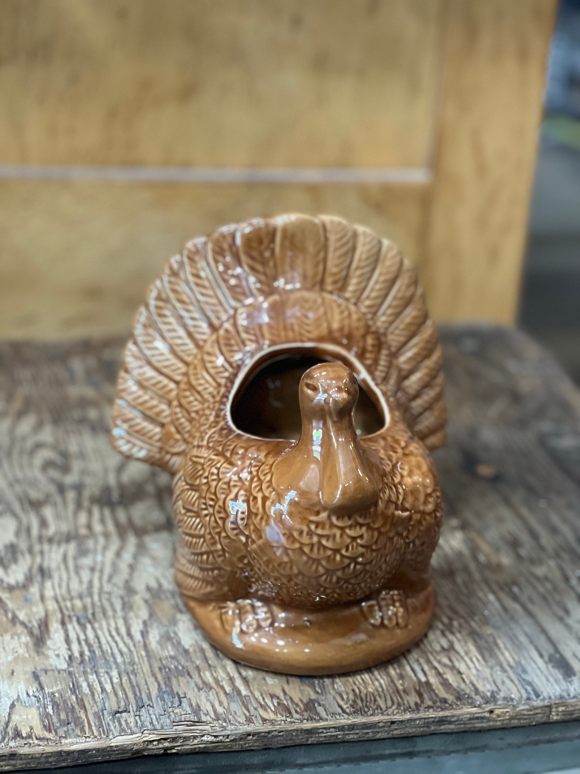 A brown glazed ceramic turkey-shaped planter with a raised fan tail and a central opening, displayed on a rustic wooden surface.
