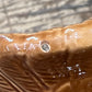 Close-up of a glossy brown ceramic surface with embossed leaf-like texture and a small circular defect or hole near the center.