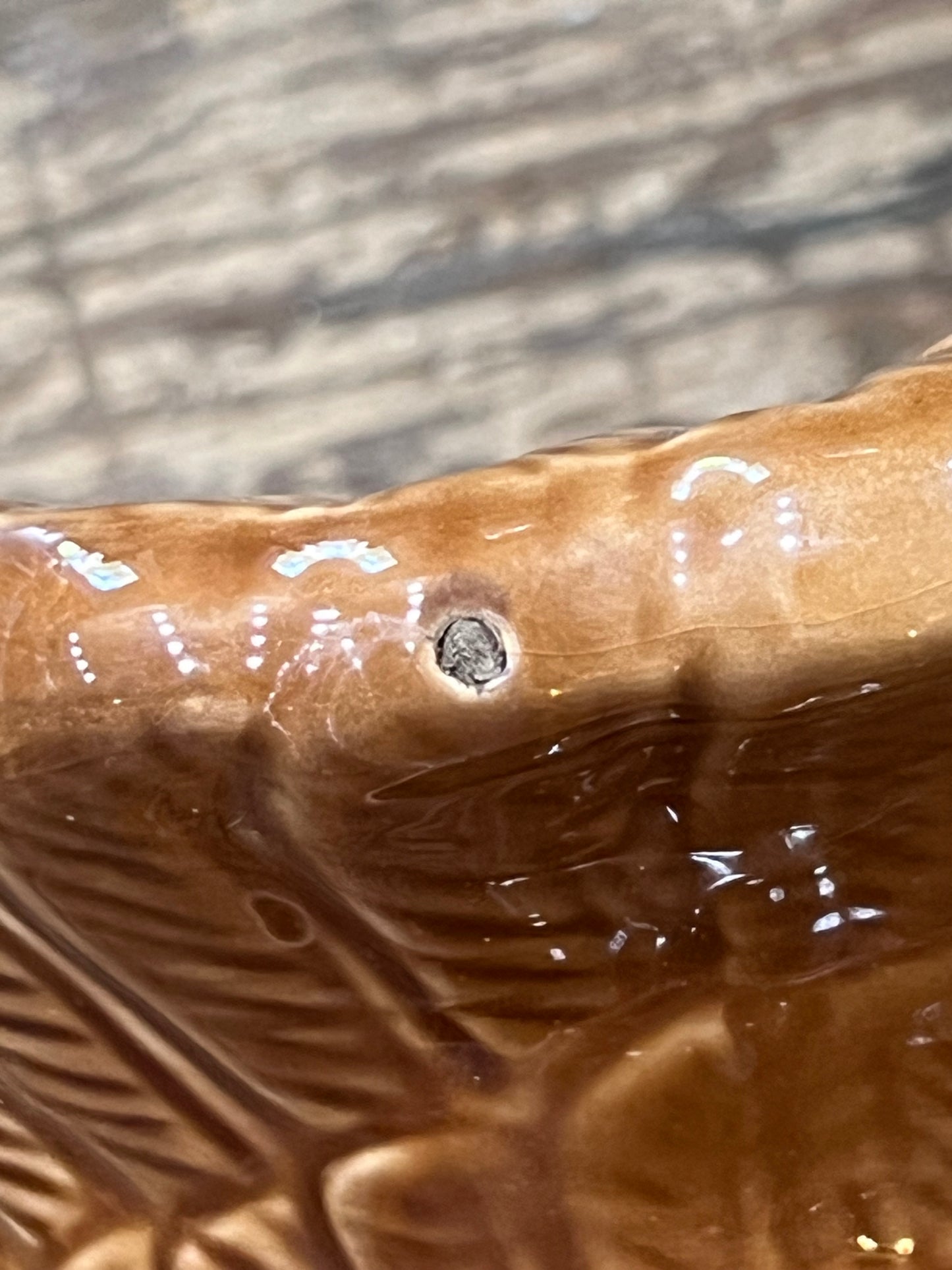 Close-up of a glossy brown ceramic surface with embossed leaf-like texture and a small circular defect or hole near the center.