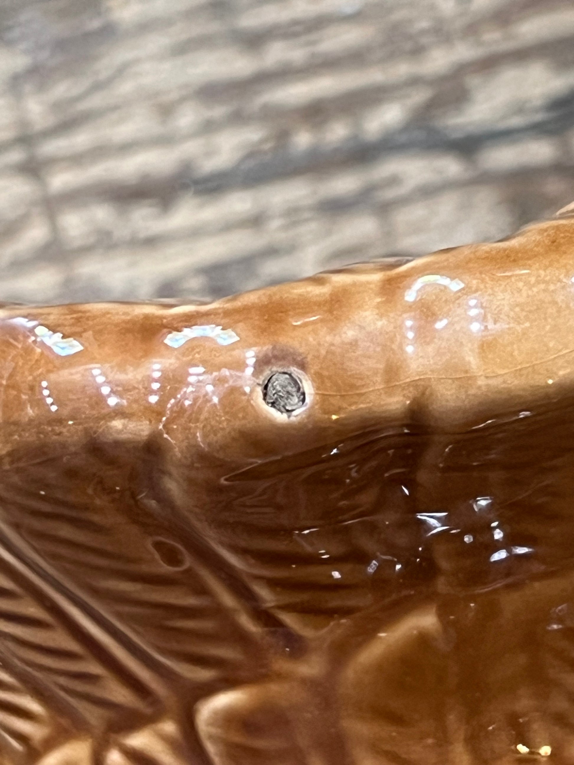 Close-up of a glossy brown ceramic surface with embossed leaf-like texture and a small circular defect or hole near the center.