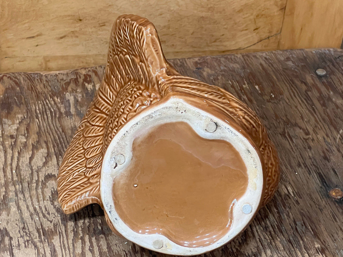 A handmade ceramic planter shaped like a bird, featuring a textured brown exterior and a glossy terracotta-colored interior, displayed on a rustic wooden surface.